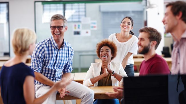 A cheerful group of employees chatting at work. Everyone is smiling and enjoying themselves.