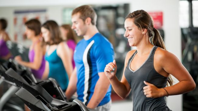 Physical activity is important for mental health. The photo shows a group of people running on treadmills at a gym. Everyone looks happy and satisfied.